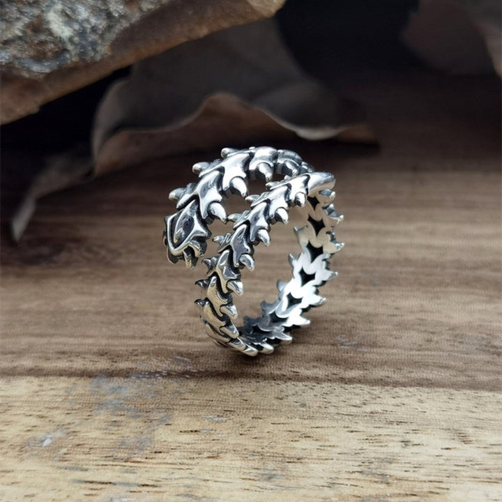 An adjustable silver-colored ring with a geometric pattern, placed on a wooden surface.